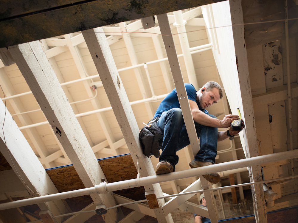 Carpenter measuring while sitting on a joist