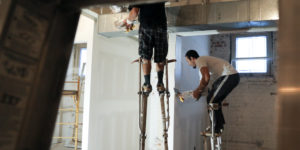 Subcontractors on stilts installing drywall