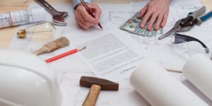 Photo of a person reviewing construction planning documents surrounded by cash and construction tools